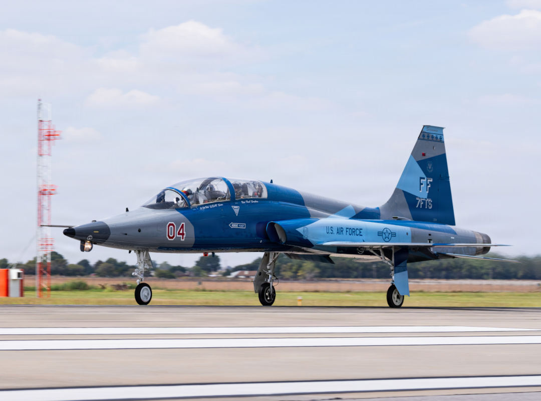U.S. Air Force T-38 Talon from Langley Air Force Base taxiing on a runway, painted in blue and gray livery with visible “FF” tail code and number 04, with landing gear down and airfield structures in the background.