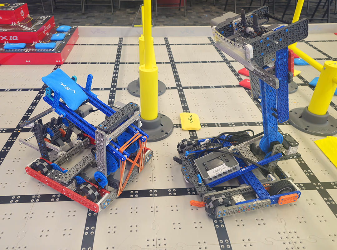 Two student-built VEX robots positioned on a competition field with colorful game elements and obstacles.