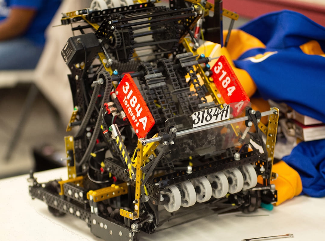 Close-up of a student-built competition robot featuring gears, rollers, structural components, and team number 3184A.