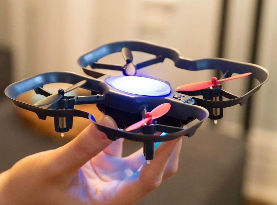 Close-up of a small four-propeller educational drone with protective rotor guards held in a person's hand.